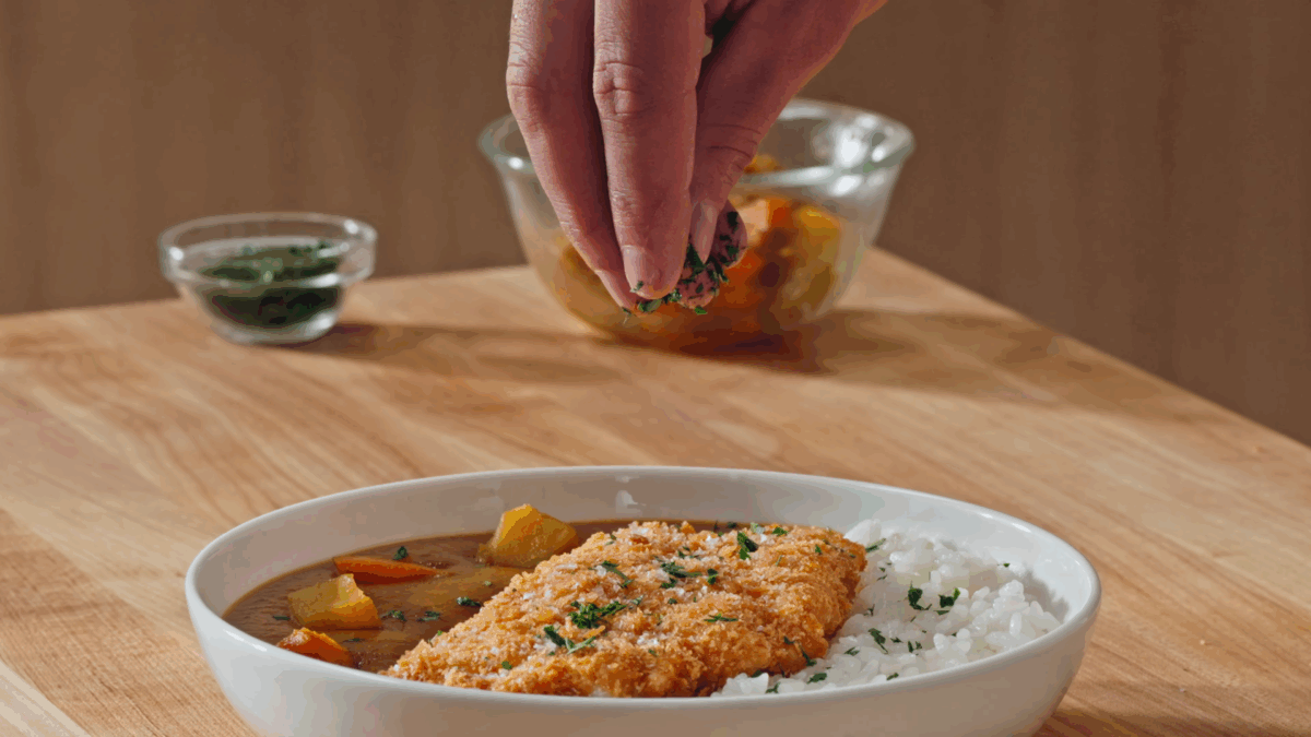 Nick DiGiovanni sprinkling fresh parsley over a bowl of Japanese rice and chicken katsu curry.