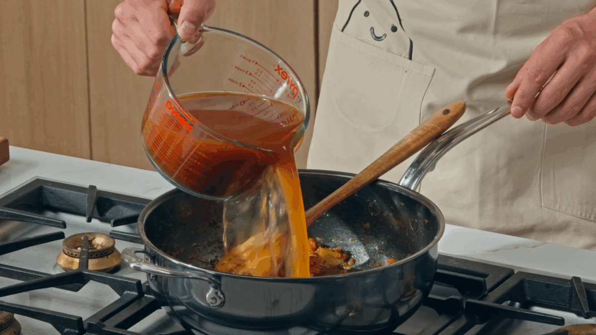 Nick DiGiovanni pouring broth into a pan of katsu curry.
