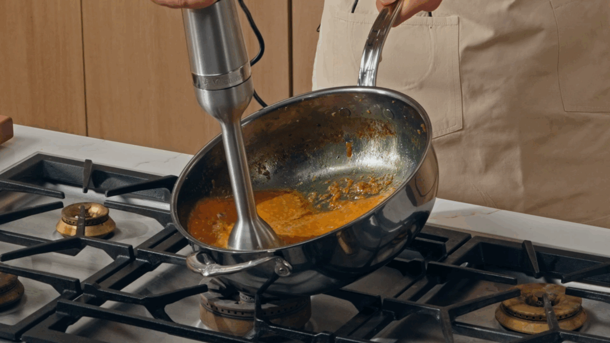 Nick DiGiovanni using an immersion blender to blend katsu curry in a pot.