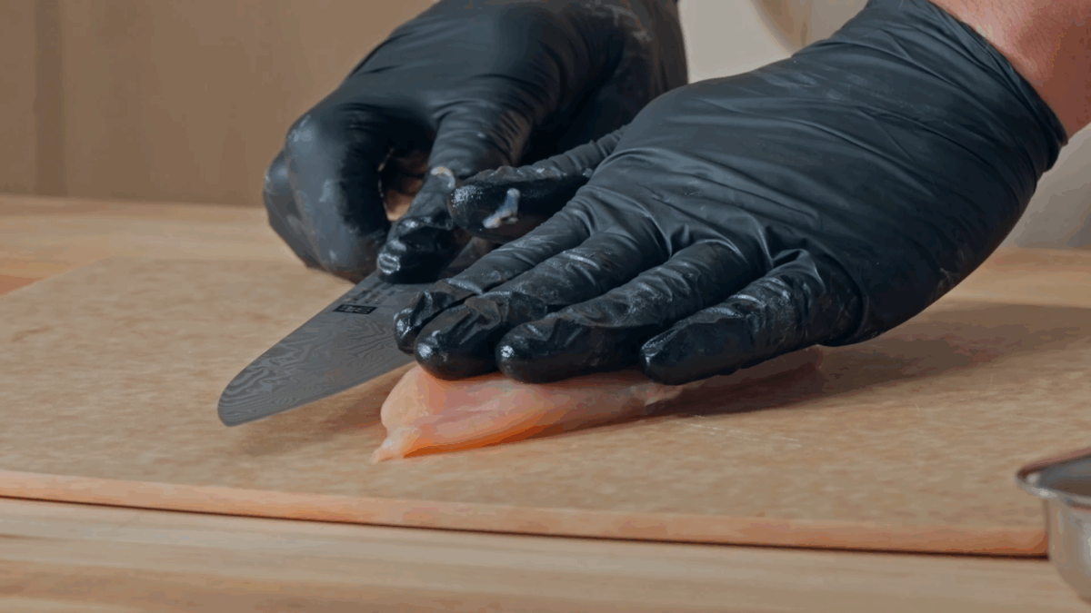 Nick DiGiovanni butterflying a chicken breast with gloved hands.