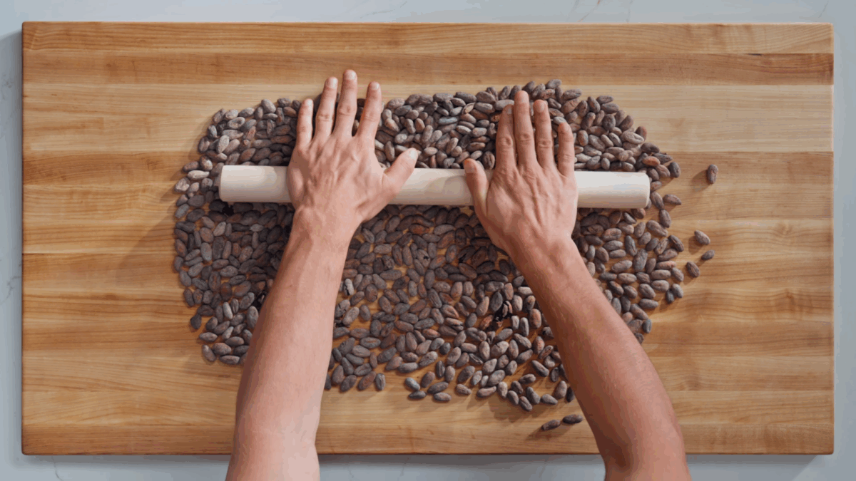 Nick DiGiovanni rolling a rolling pin over roasted cacao beans. 