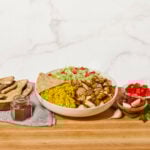 A bowl of halal chicken with yellow rice, lettuce, tomatoes, white sauce, red sauce, and pita bread.