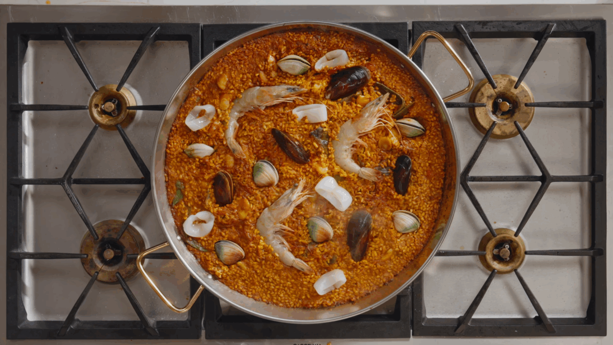 Seafood paella simmering in a pan on the stovetop. 