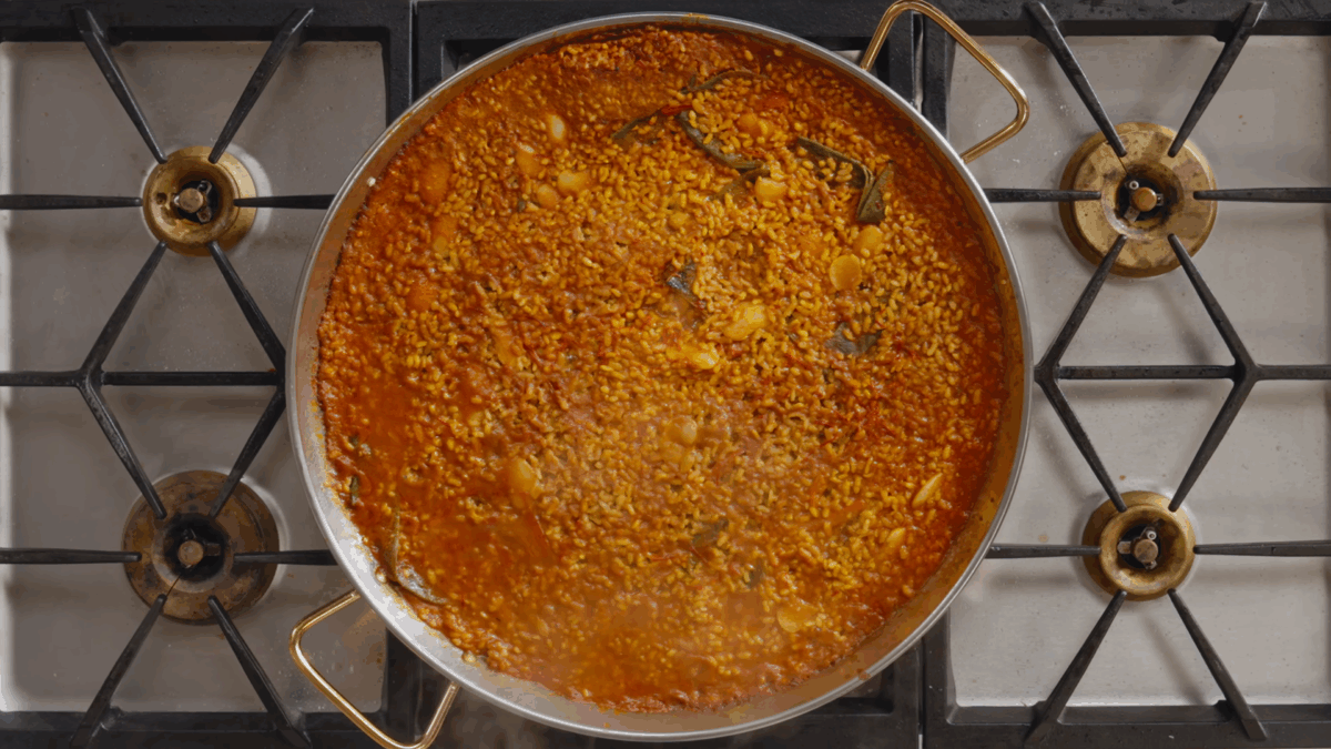 Seafood paella simmering in a pot on the stovetop. 