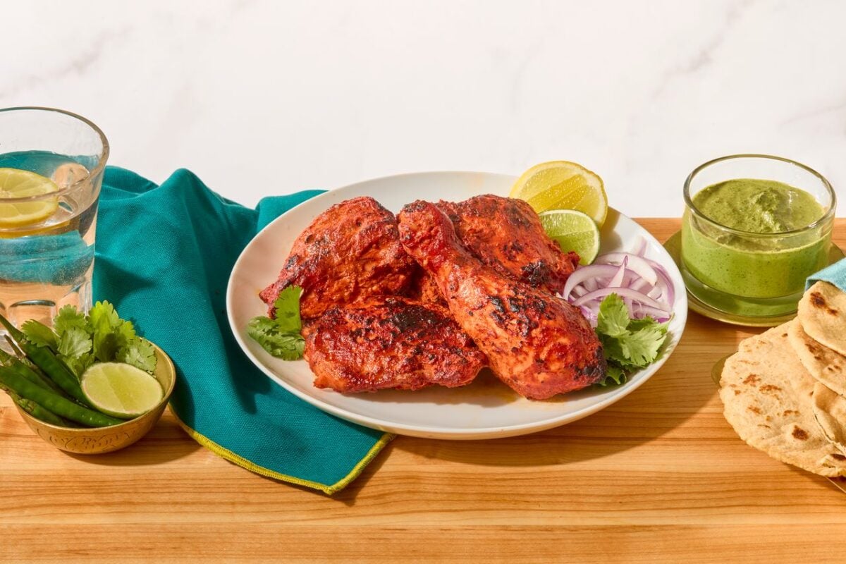 A plate of tandoori chicken next to a bowl of mint-coriander chutney and naan.