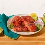 A plate of tandoori chicken next to a bowl of mint-coriander chutney and naan.