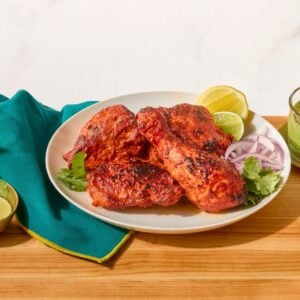 A plate of tandoori chicken next to a bowl of mint-coriander chutney and naan.