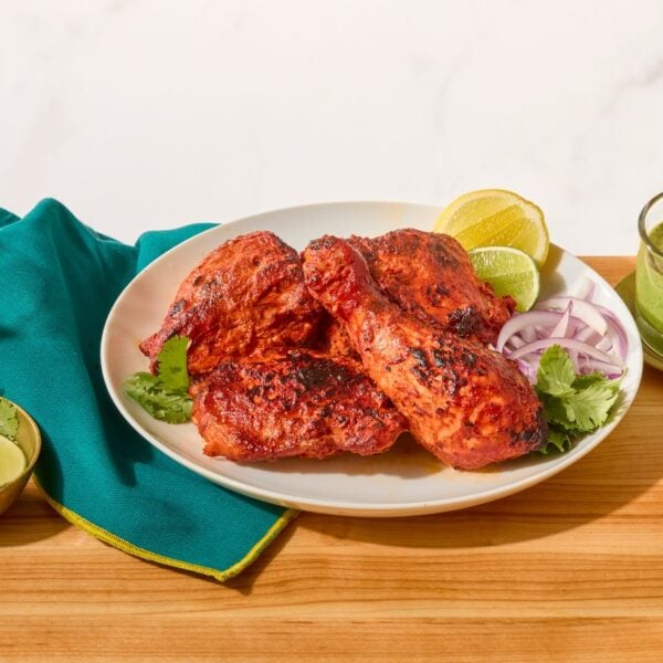 A plate of tandoori chicken next to a bowl of mint-coriander chutney and naan.