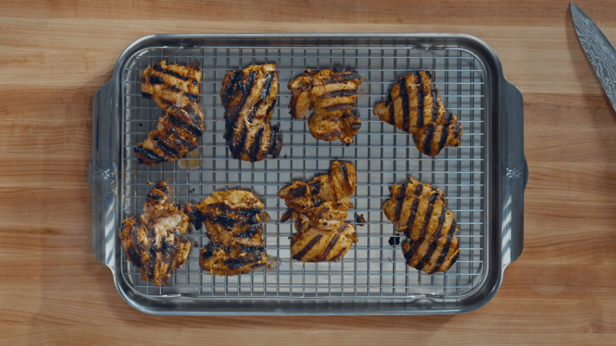 Eight halal chicken thighs resting on a wire rack lined baking sheet.