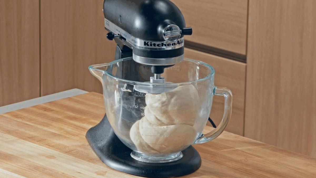 Homemade bagel dough being combined in the bowl of a stand mixer. 