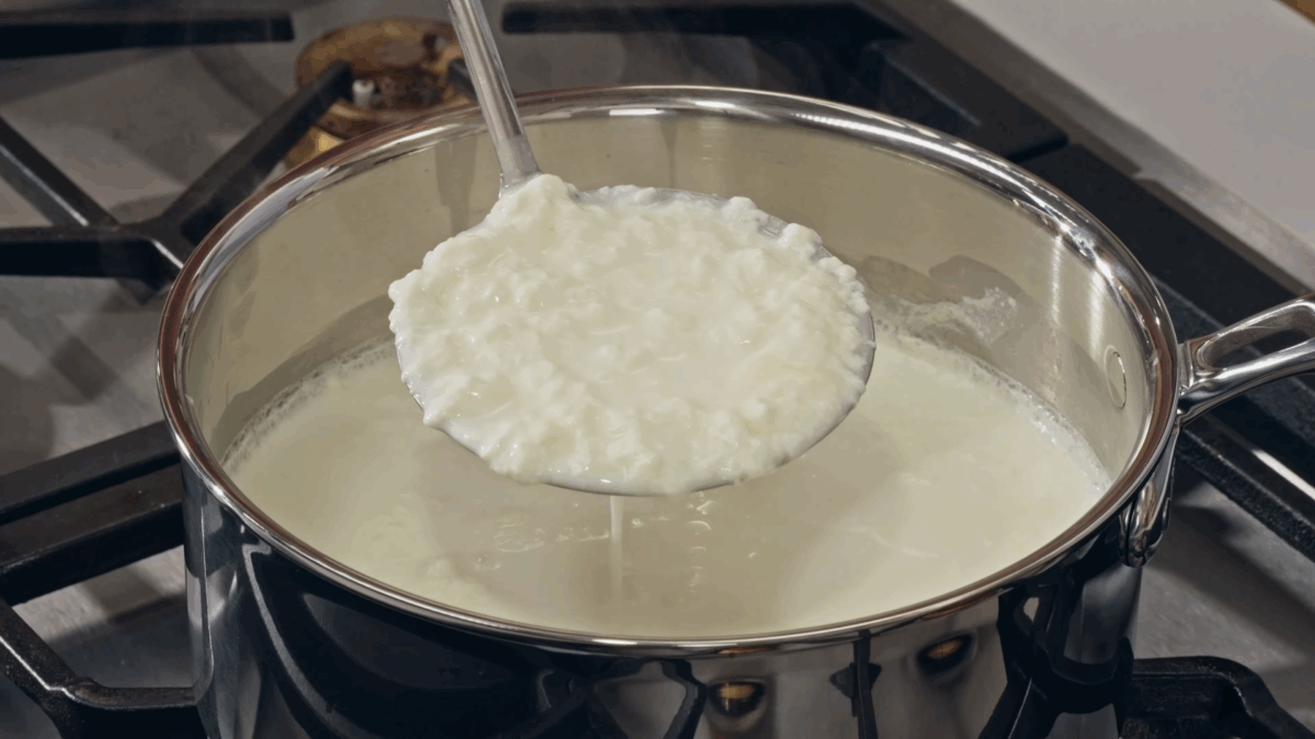 Milk and cream being heated on the stove, forming curds. 