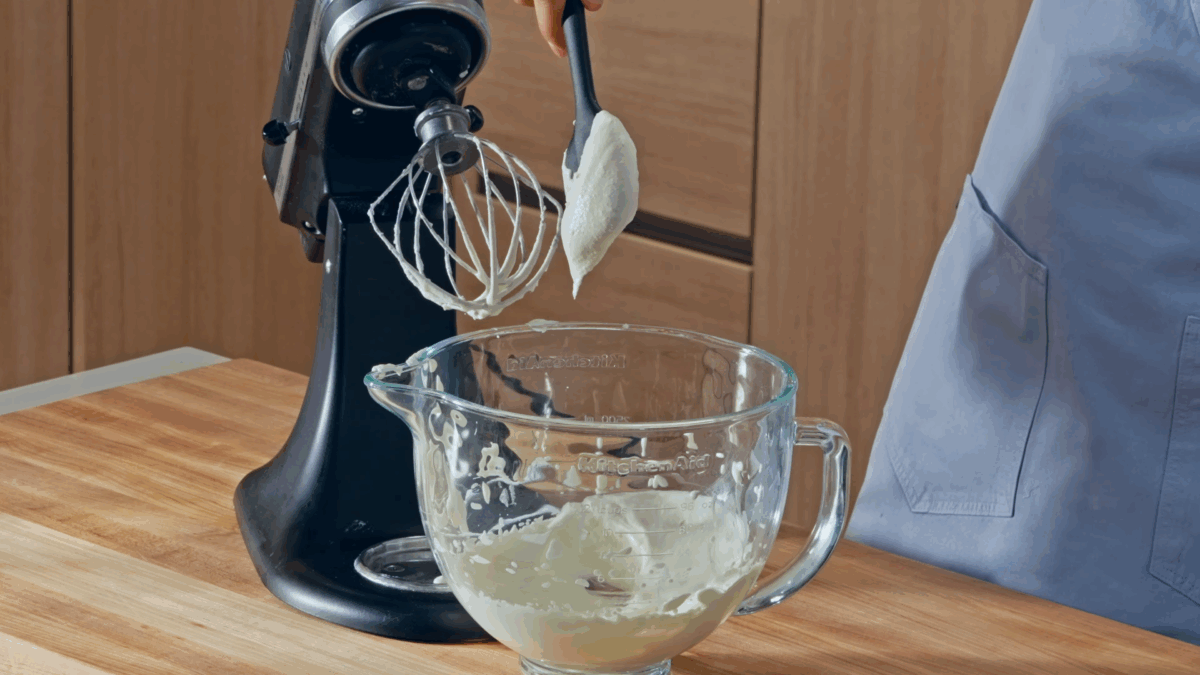 Nick DiGiovanni using a spatula to lift homemade cream cheese from the bowl of a stand mixer. 