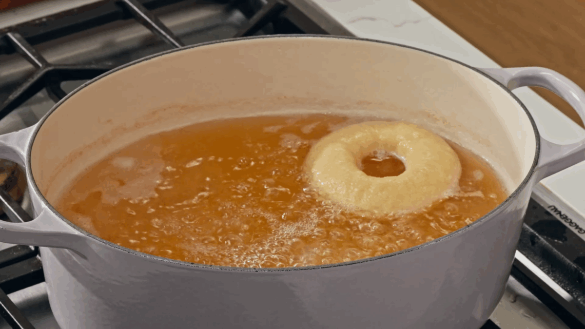 A homemade bagel boiling in a pot of water. 