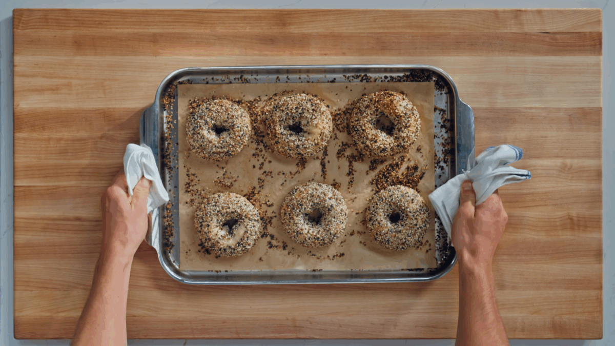 Nick DiGiovanni holding a baking sheet with six New York-style homemade bagels topped with everything bagel seasoning. 
