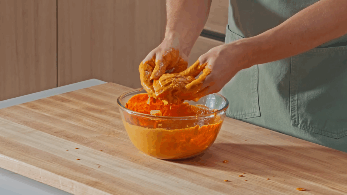 Nick DiGiovanni using his hands to rub tandoori marinade into raw chicken. 