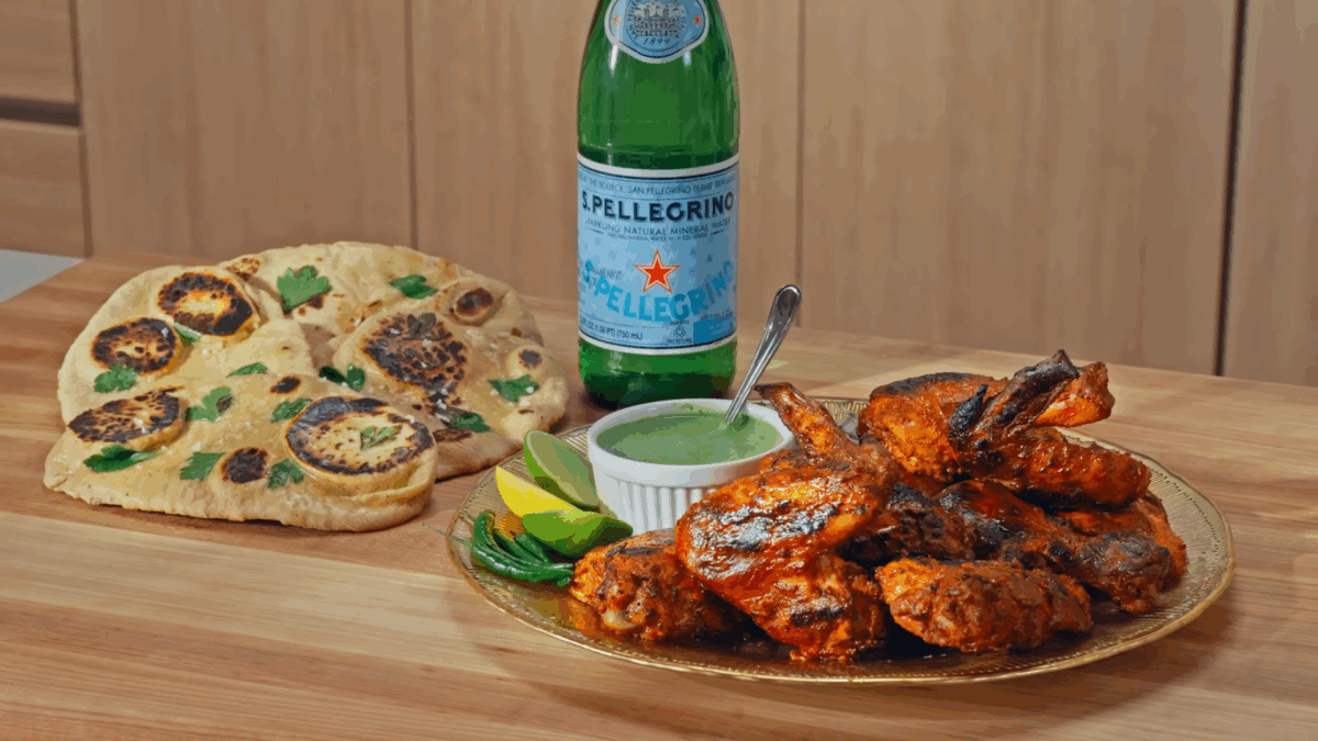 A plate of tandoori chicken, mint-coriander chutney, and naan next to a bottle of S. Pellegrino.