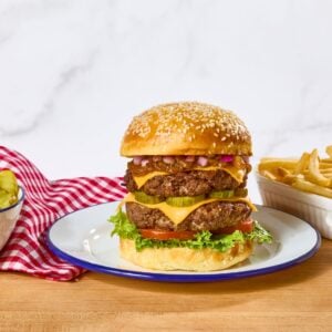 A double cheeseburger on a plate next to a bowl of pickles and fries.