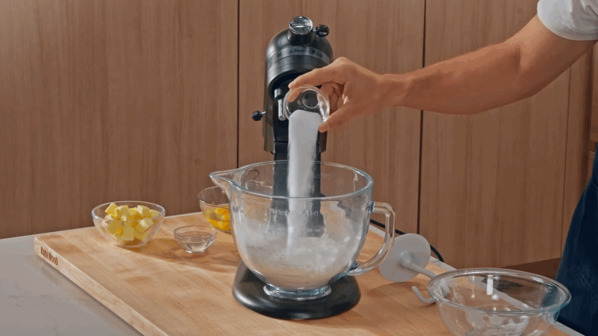 Nick DiGiovanni combining hamburger bun ingredients in the bowl of a stand mixer fitted iwth a dough hook.