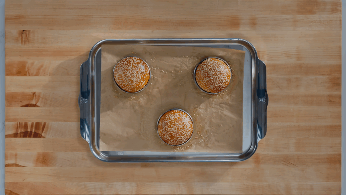 Three baked hamburger buns on a parchment paper-lined baking sheet.
