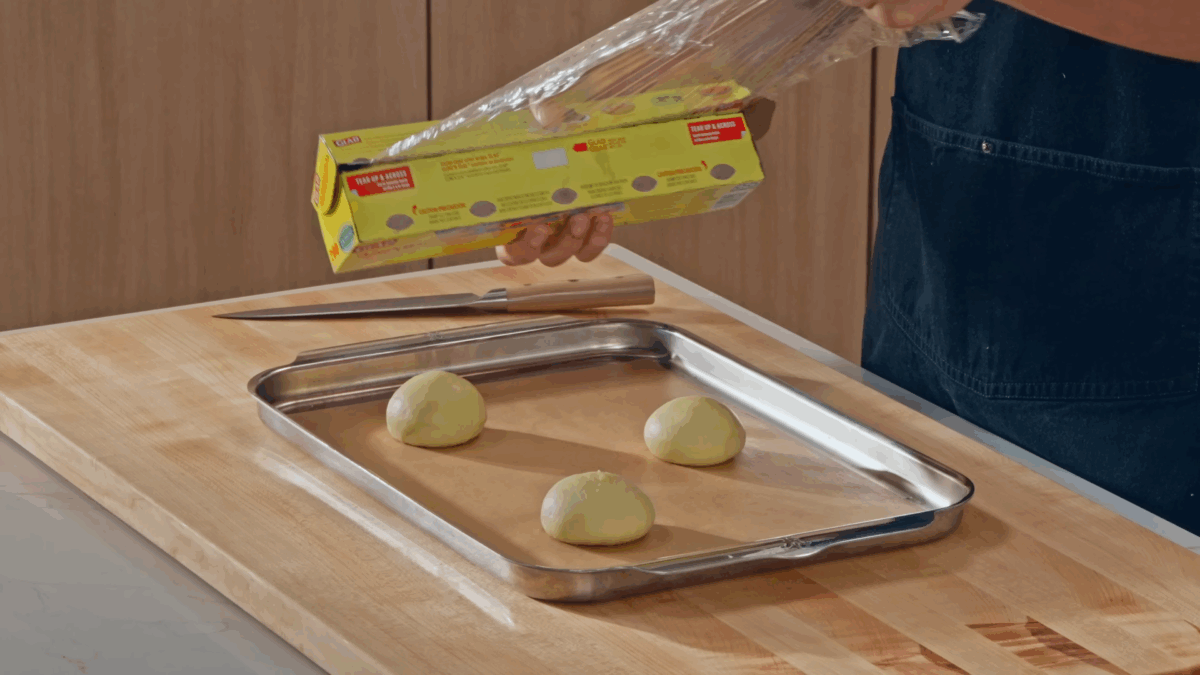 Three balls of hamburger bun dough on a parchment paper-lined baking sheet.