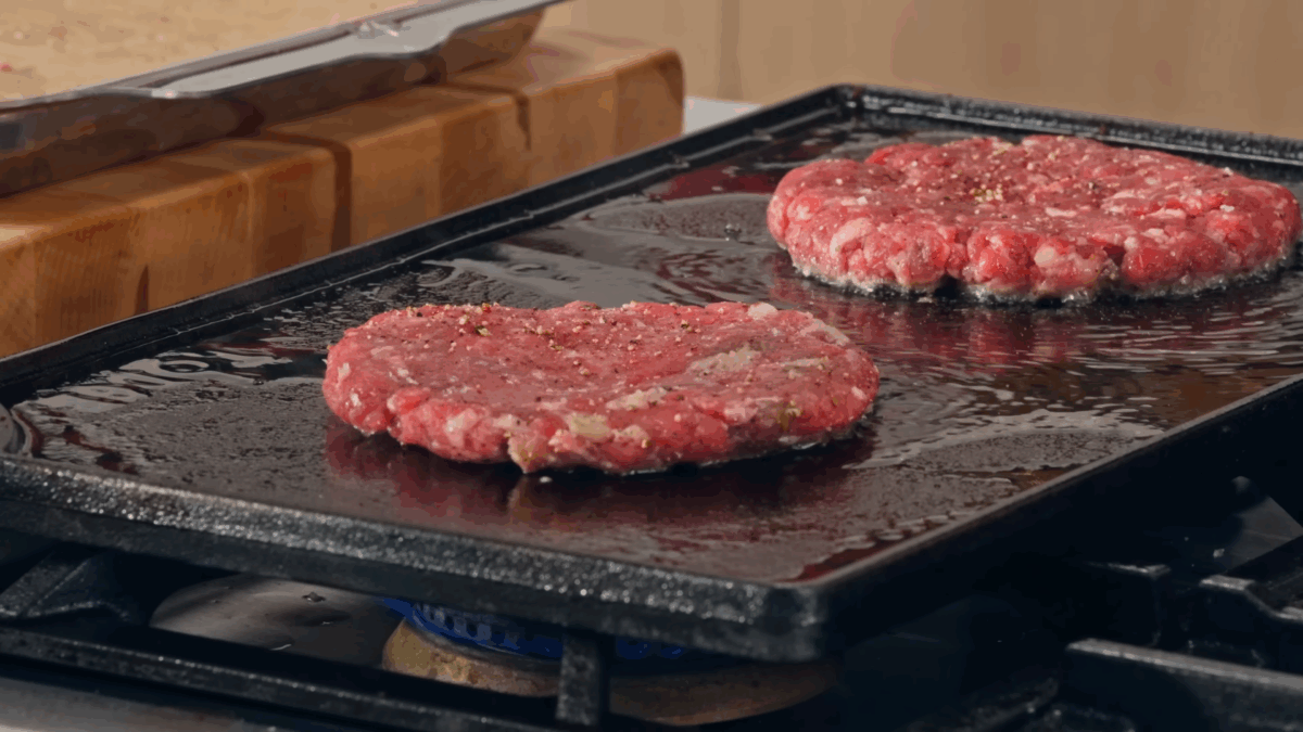 Two hamburger patties cooking on a flat top.