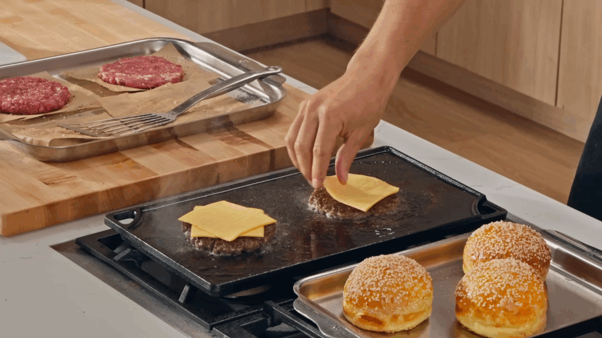 Nick DiGiovanni placing slices of cheese on burger patties cooking on a flat top grill.