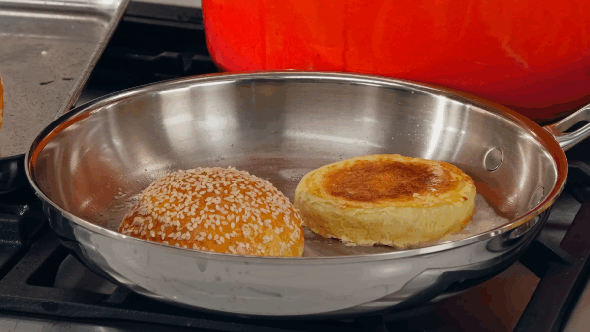 A homemade burger bun toasting in a skillet.