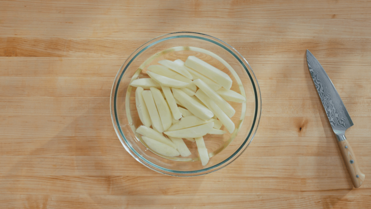 Potato slices soaking in a bowl of water.