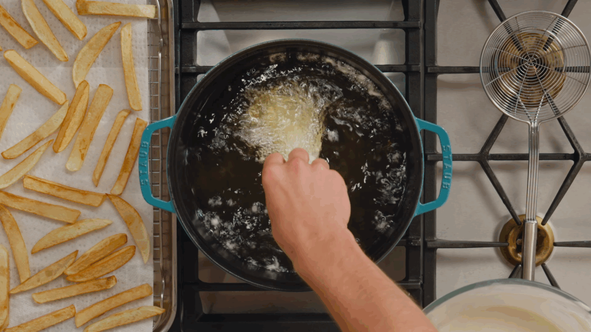 Nick DiGiovanni placing a breaded piece of cod into a Dutch oven of oil.