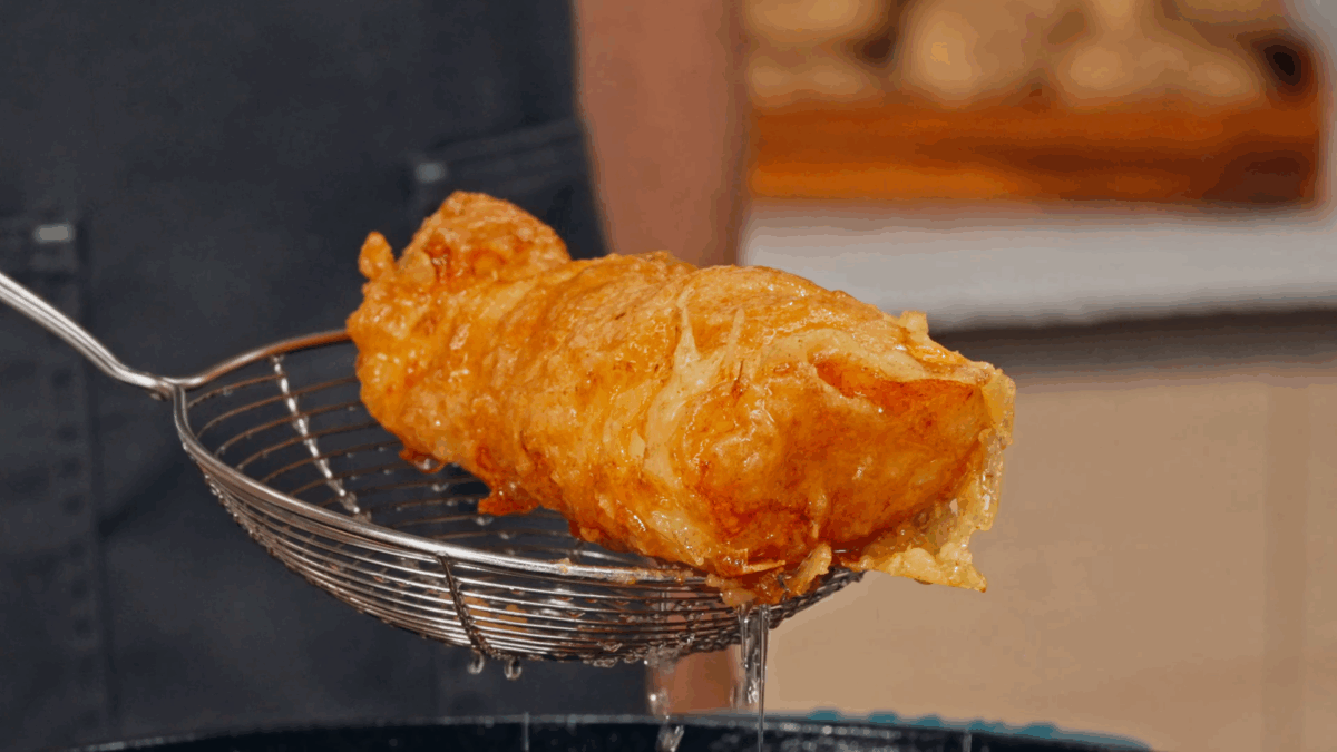 Nick DiGiovanni using a spider to lift a piece of fried cod from a pot.