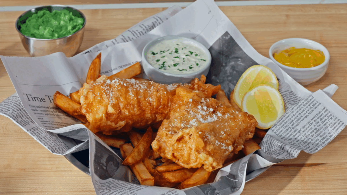A basket of homemade fish and chips with tartar sauce, U.K. curry sauce, and mashed peas.