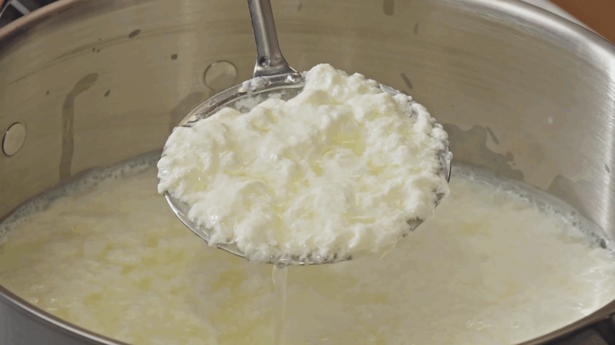 Nick DiGiovanni lifting a scoop of curds and whey from a pot. 