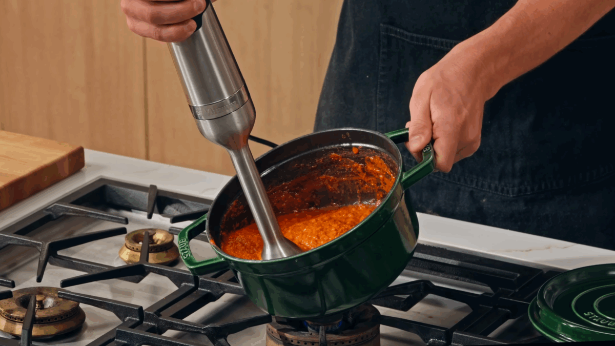 Nick DiGiovanni using an immersion blender to blend butter masala gravy. 