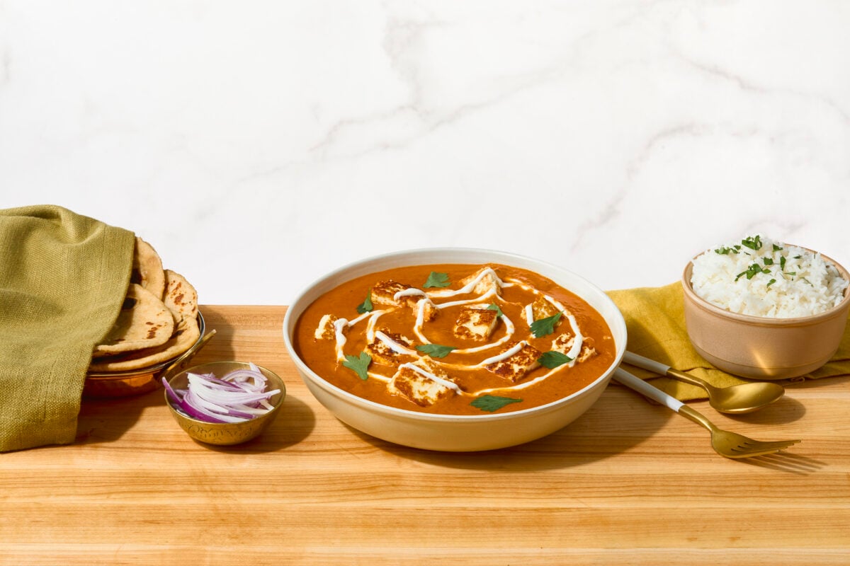 A bowl of paneer butter masala next to a plate of naan and a bowl of rice.