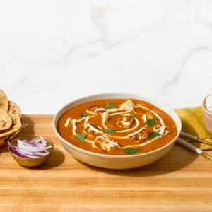 A bowl of paneer butter masala next to a plate of naan and a bowl of rice.