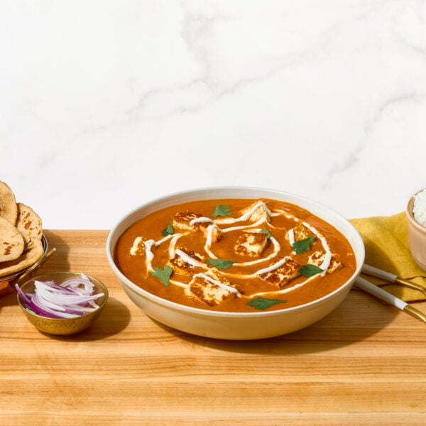 A bowl of paneer butter masala next to a plate of naan and a bowl of rice.