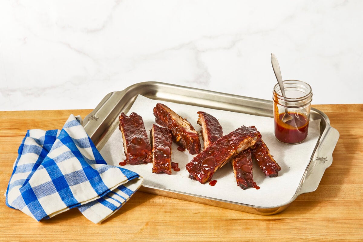 St. Louis style ribs on a sheet tray with a jar of BBQ sauce.