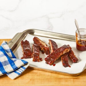 St. Louis style ribs on a sheet tray with a jar of BBQ sauce.