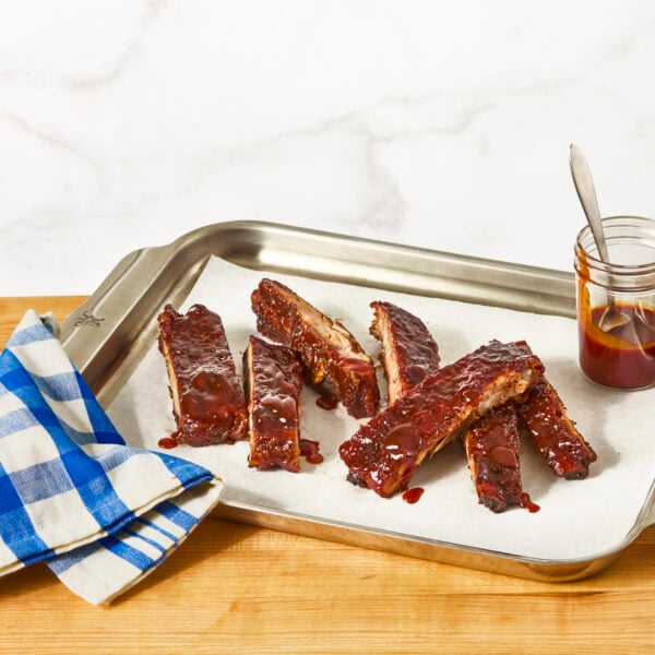 St. Louis style ribs on a sheet tray with a jar of BBQ sauce.