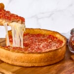 A deep dish pizza on a counter, a slice being lifted.
