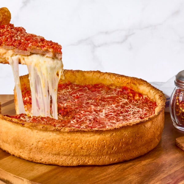 A deep dish pizza on a counter, a slice being lifted.