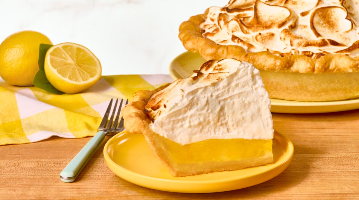 A slice of lemon meringue pie next to the rest of the pie in a pan.
