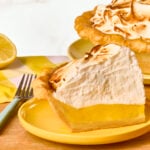 A slice of lemon meringue pie next to the rest of the pie in a pan.