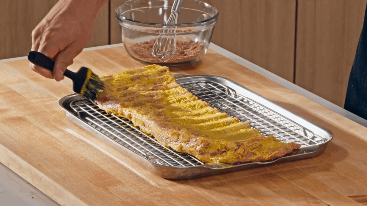 Nick DiGiovanni brushing mustard over a rack of ribs.