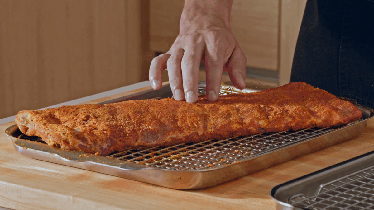 Nick DiGiovanni tapping a seasoned and rested rack of St. Louis style pork ribs.