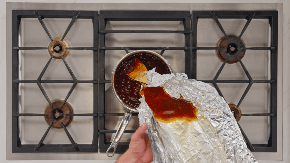 Nick DiGiovanni adding pork rib drippings to a pot of BBQ sauce on the stovetop.