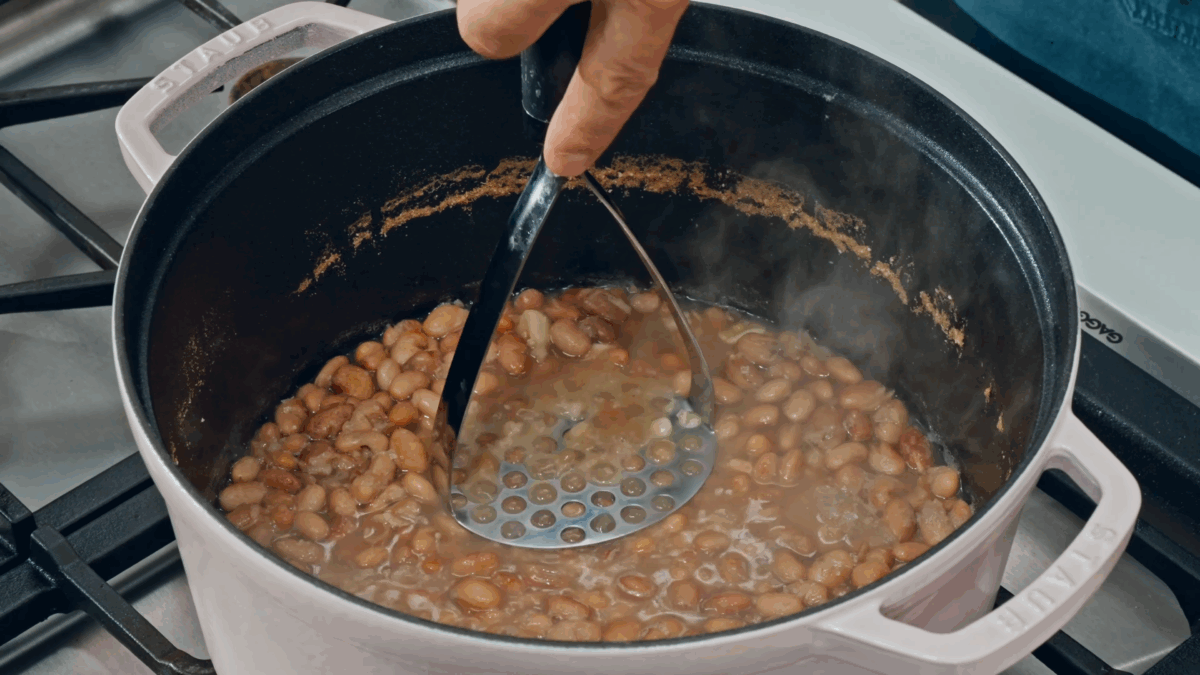 Nick DiGiovanni using a masher to smash cooked pinto beans in a Dutch oven. 