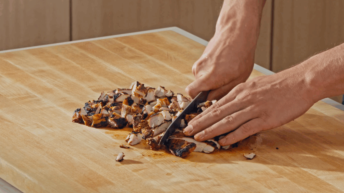 Nick DiGiovanni chopping  cooked chicken thighs into bite-sized pieces. 