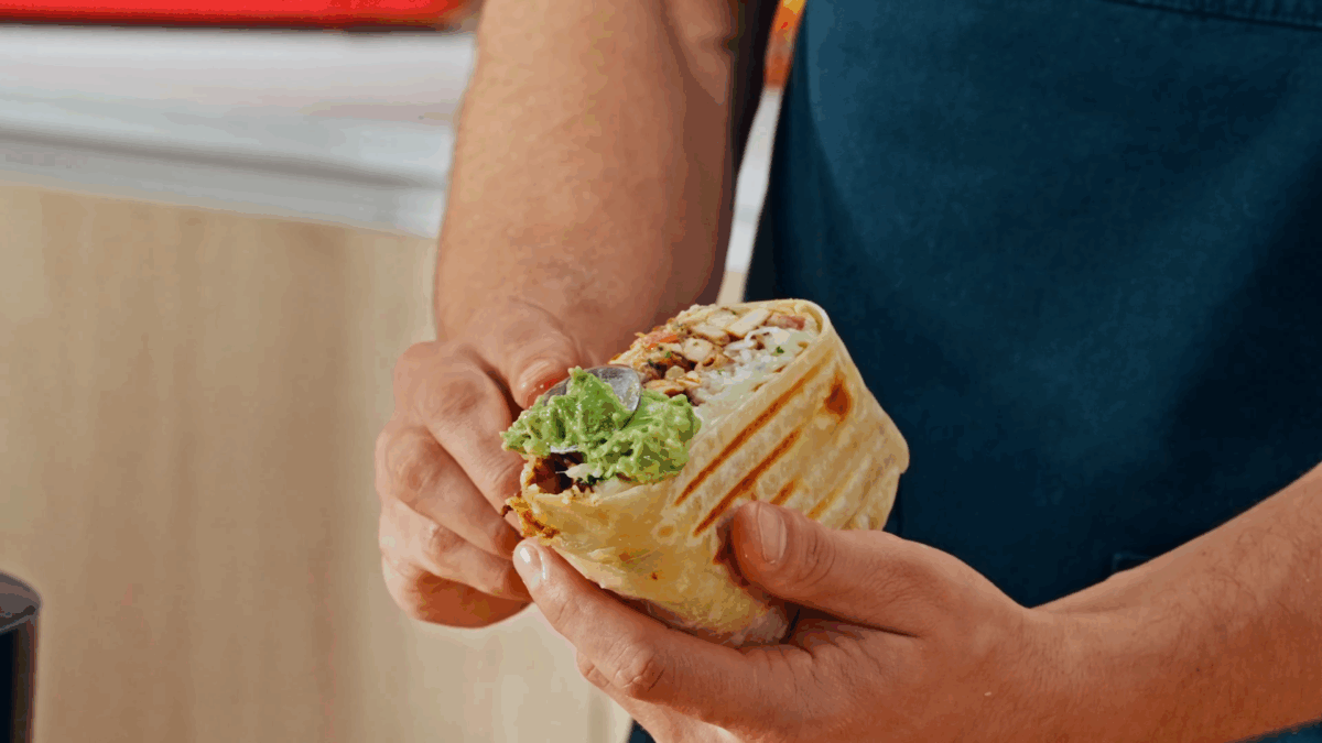Nick DiGiovanni spooning guacamole over half a chicken burrito. 