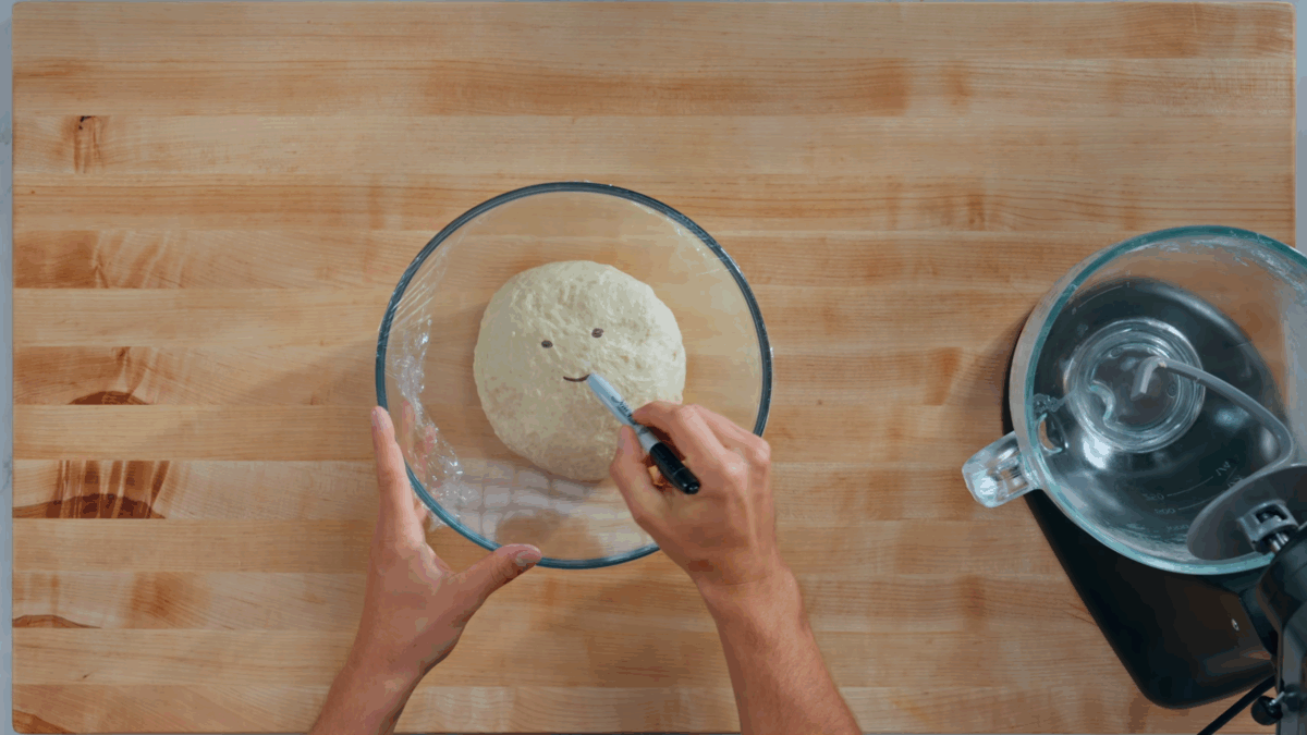 Nick DiGiovanni drawing a smiley face on plastic wrap covering deep dish pizza dough in a bowl.